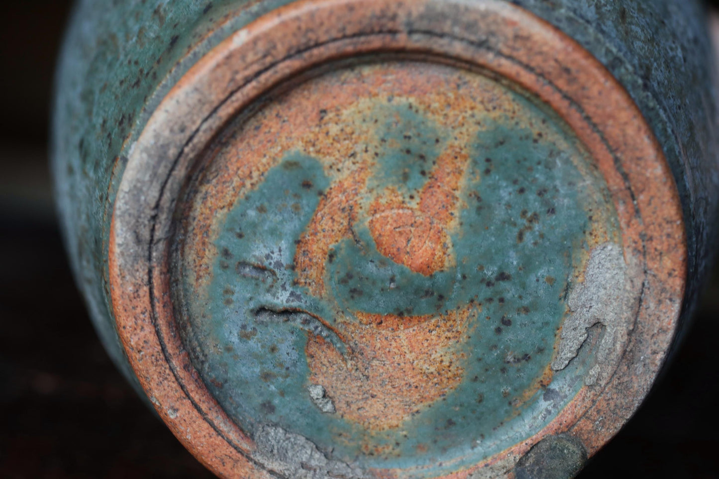 A close-up view of a ceramic vase or container with a textured surface, featuring a pattern of orange and green colors.