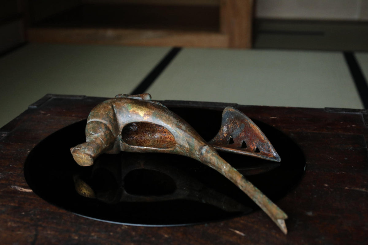 An old, rusted metal object resembling a fish or sea creature is resting on a black circular surface.