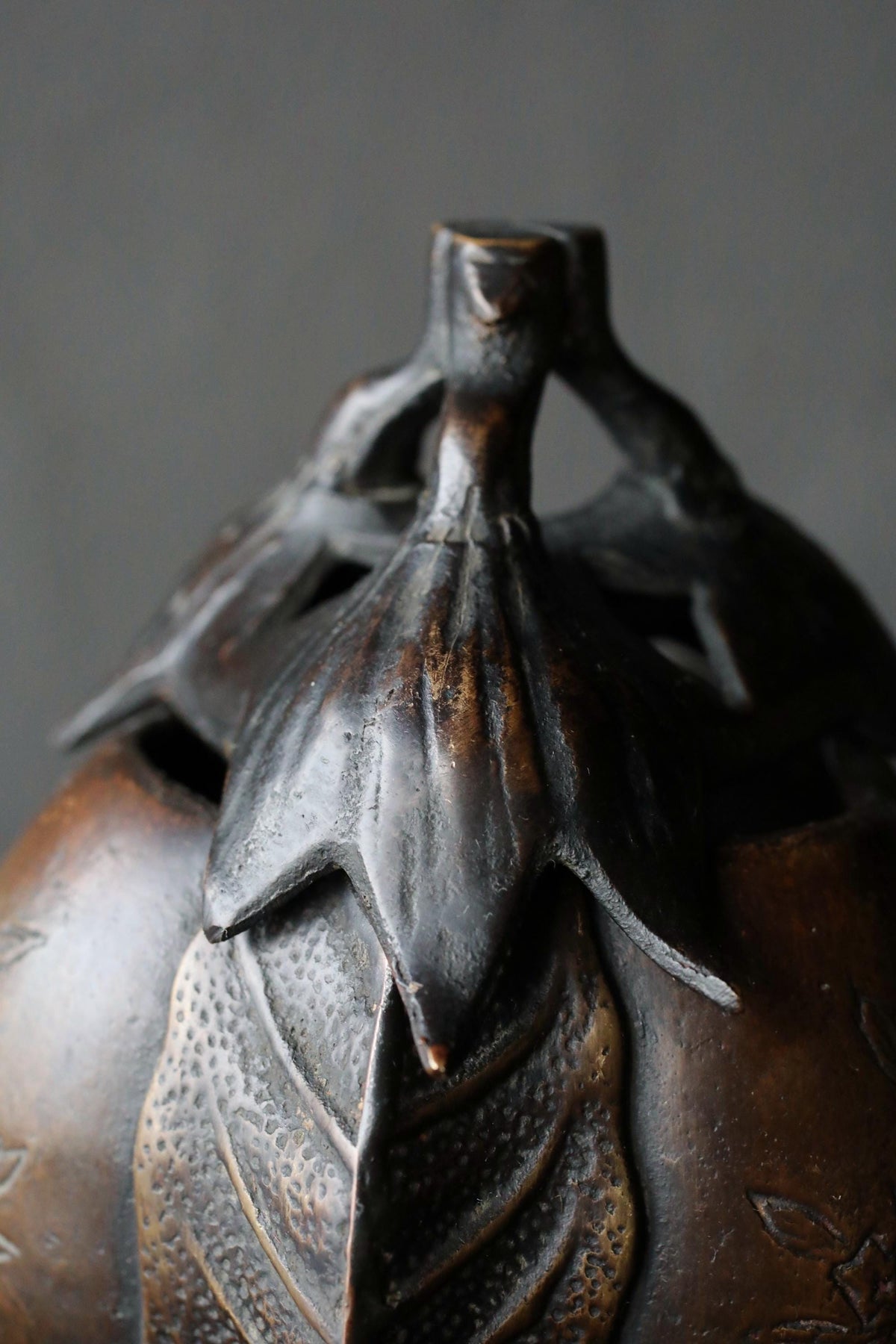 A close-up view of a dark brown metal sculpture with a leaf-like design, featuring a small opening at the top.
