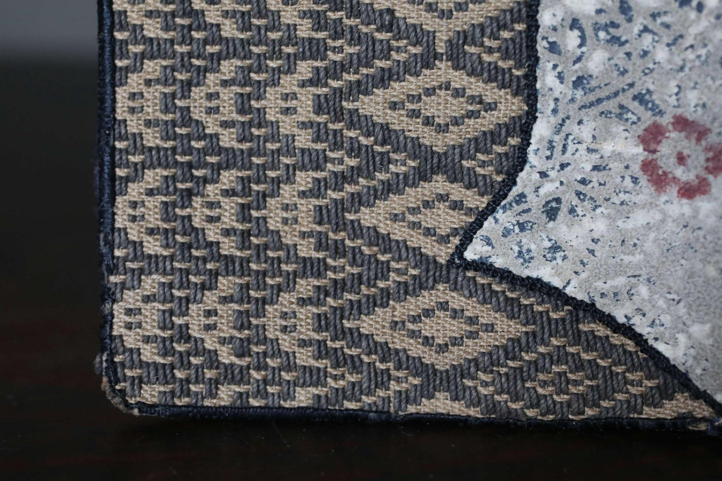 a close-up view of a woven fabric with a diamond pattern, featuring a mix of black, gray, and beige colors.