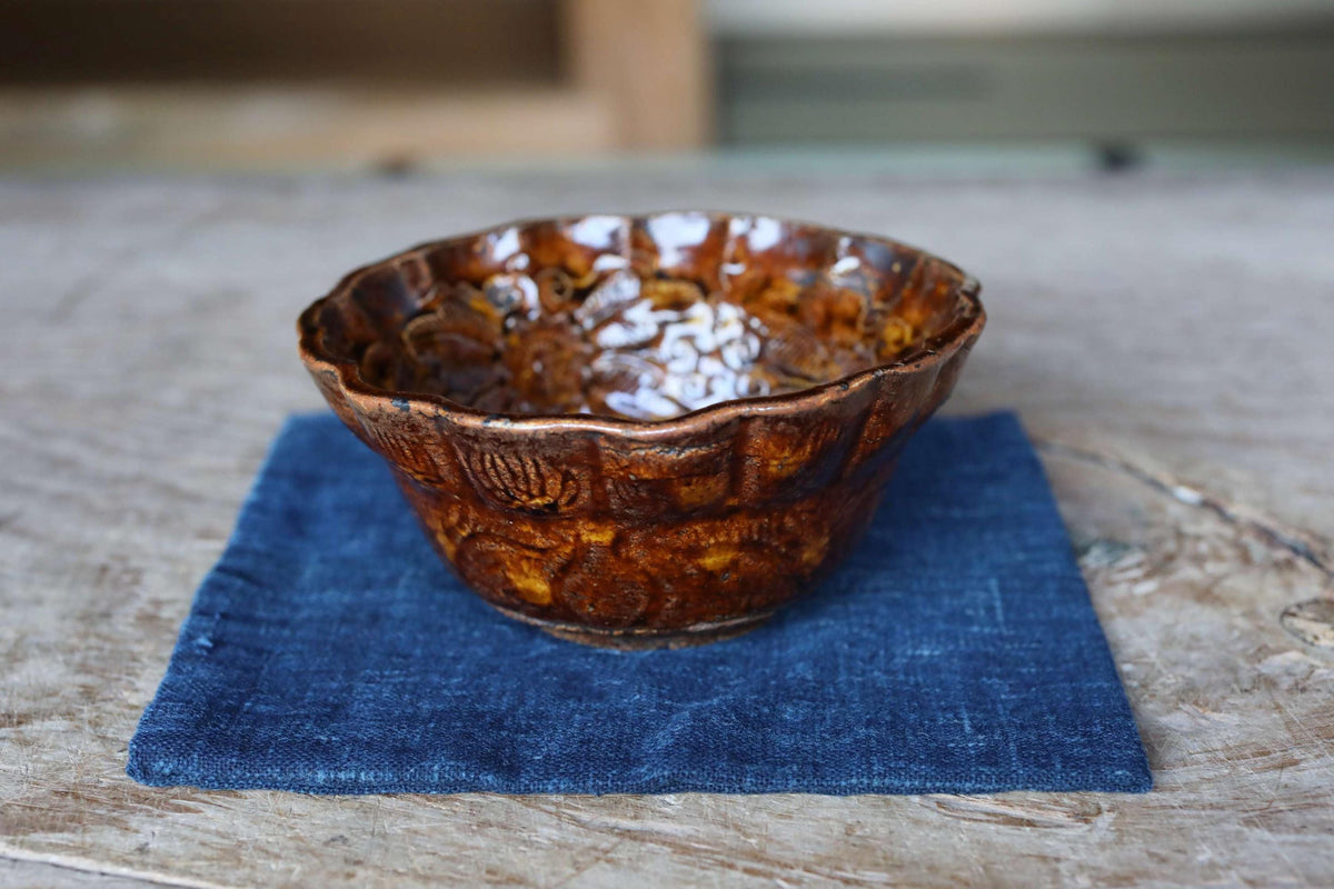 A brown ceramic bowl with a scalloped edge sits on a blue cloth on a wooden surface.