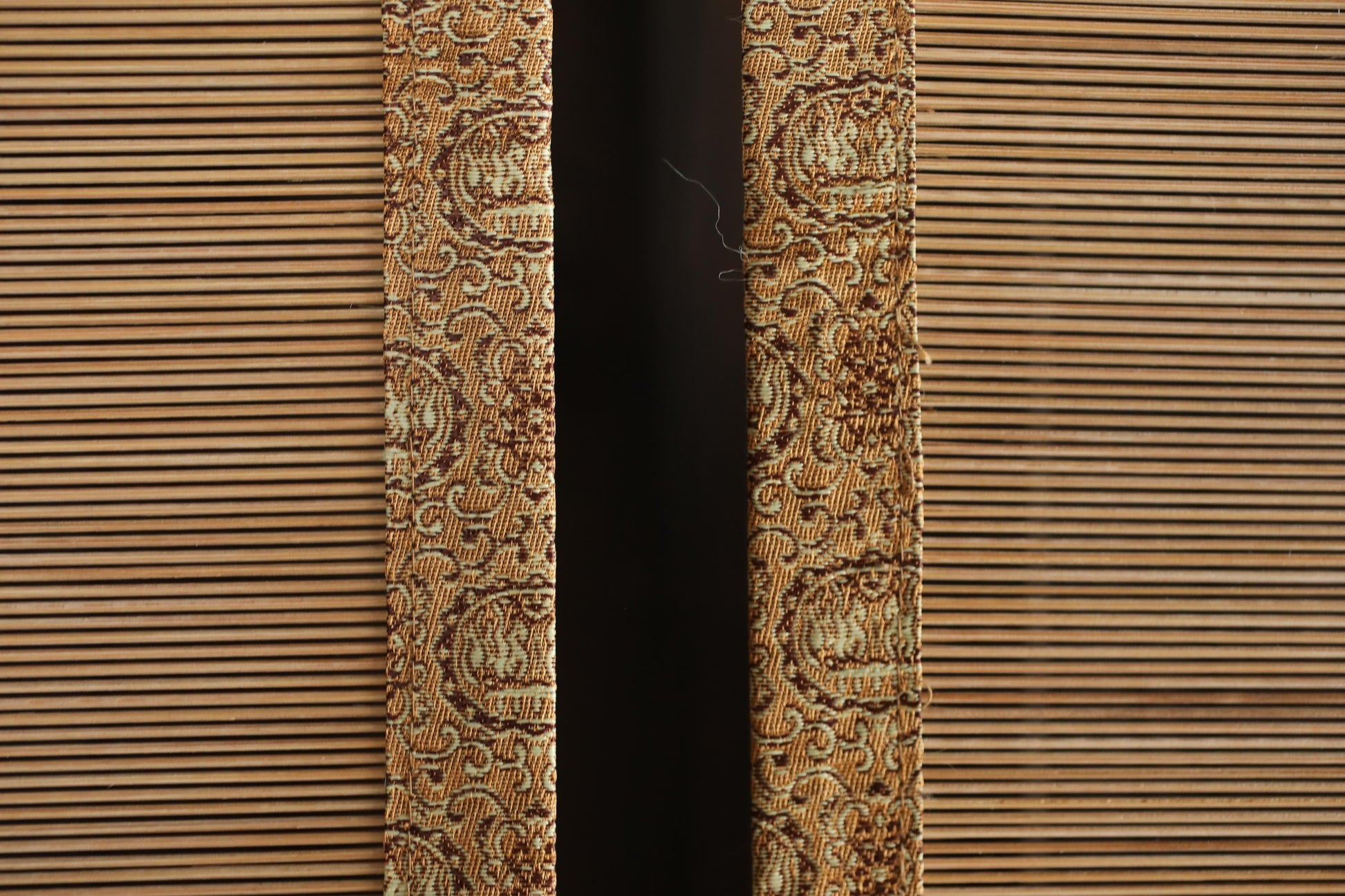 a close-up view of a patterned fabric, possibly a curtain or textile, with a dark background.