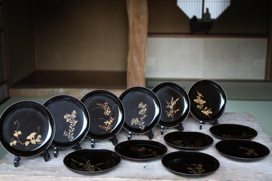 A collection of black plates with gold floral designs, arranged on a wooden surface.