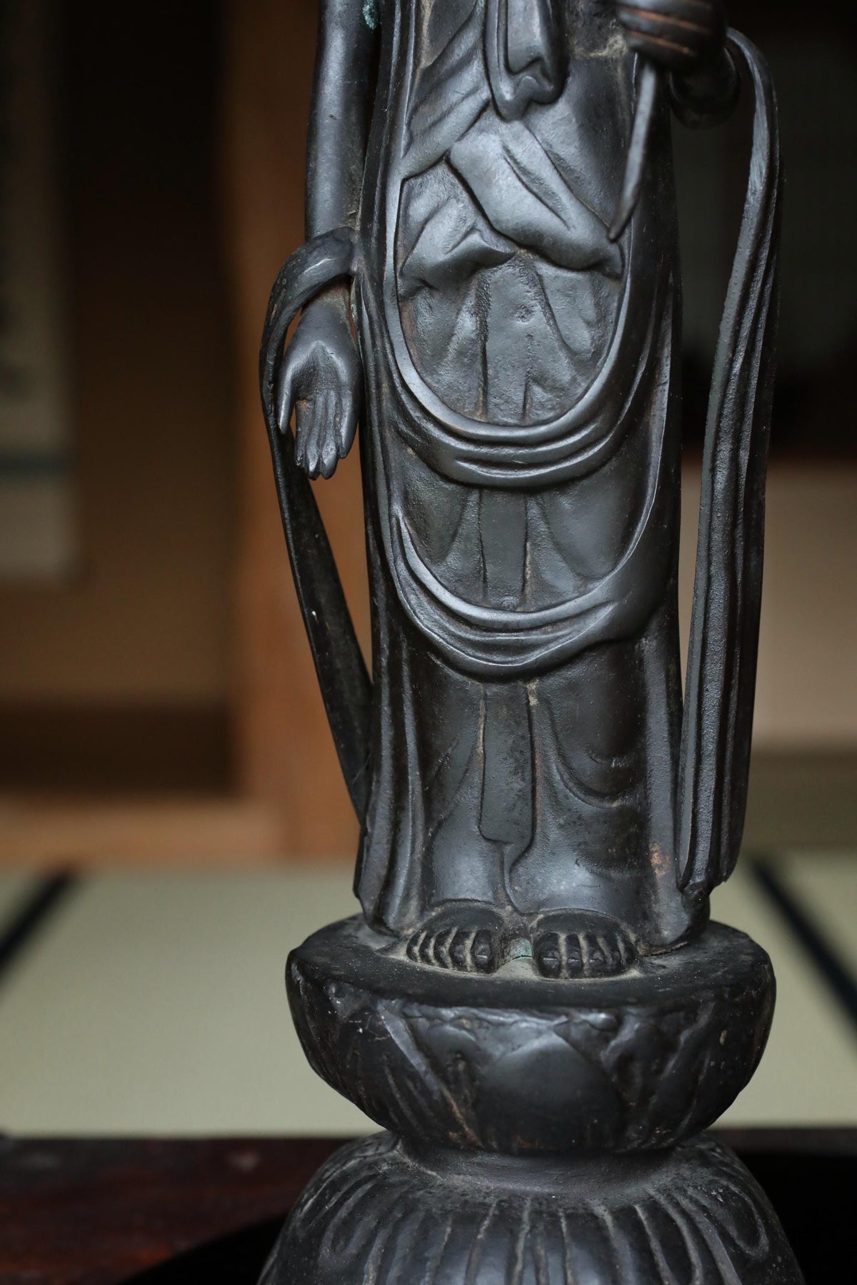 A close-up view of a dark-colored statue or sculpture, possibly of a deity or religious figure, standing on a pedestal or base.