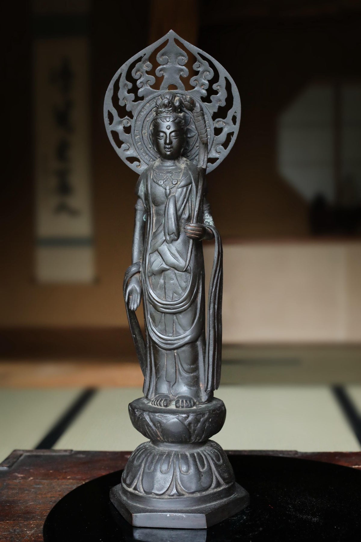 A bronze statue of a Buddhist deity, likely a Buddha, standing on a pedestal with intricate designs around the head.