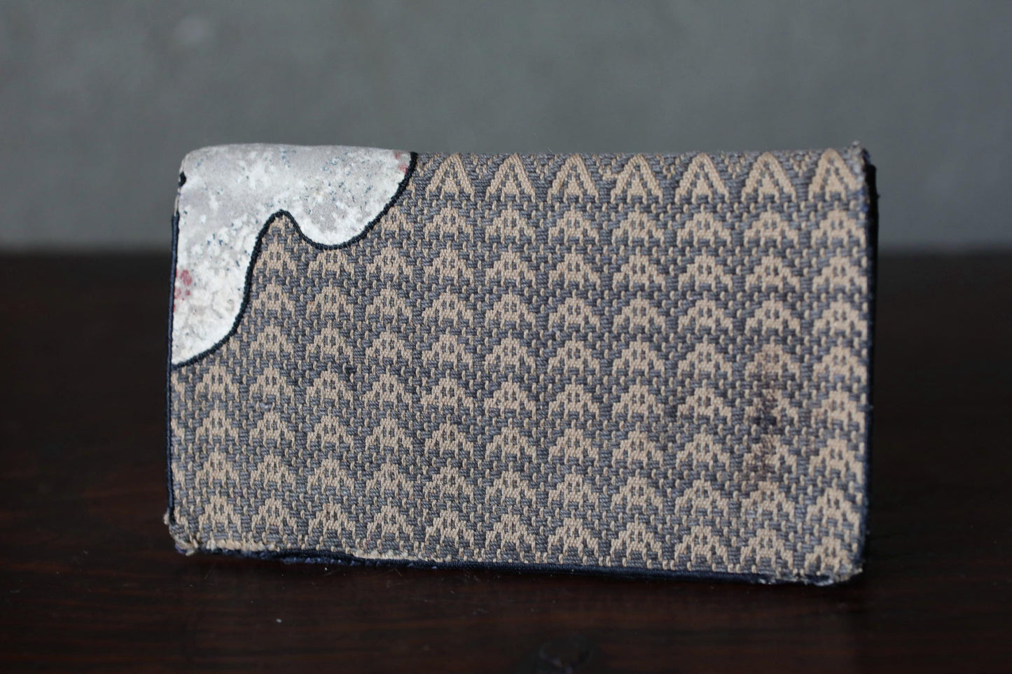 A wallet with a woven pattern and a small white object on the left side.