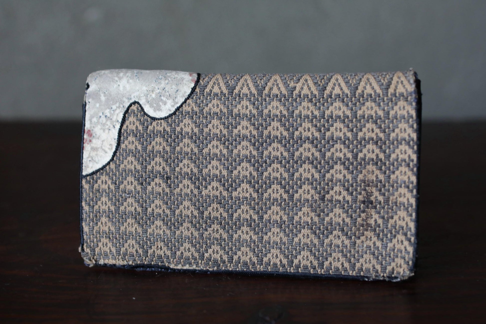 A wallet with a woven pattern and a small white object on the left side.
