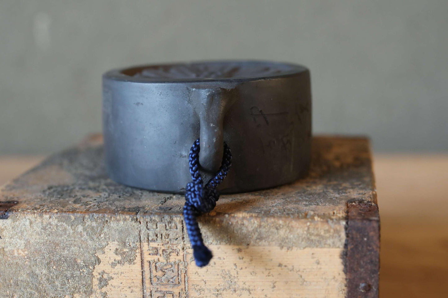 A black metal object with a blue string hanging from it, placed on a wooden surface.