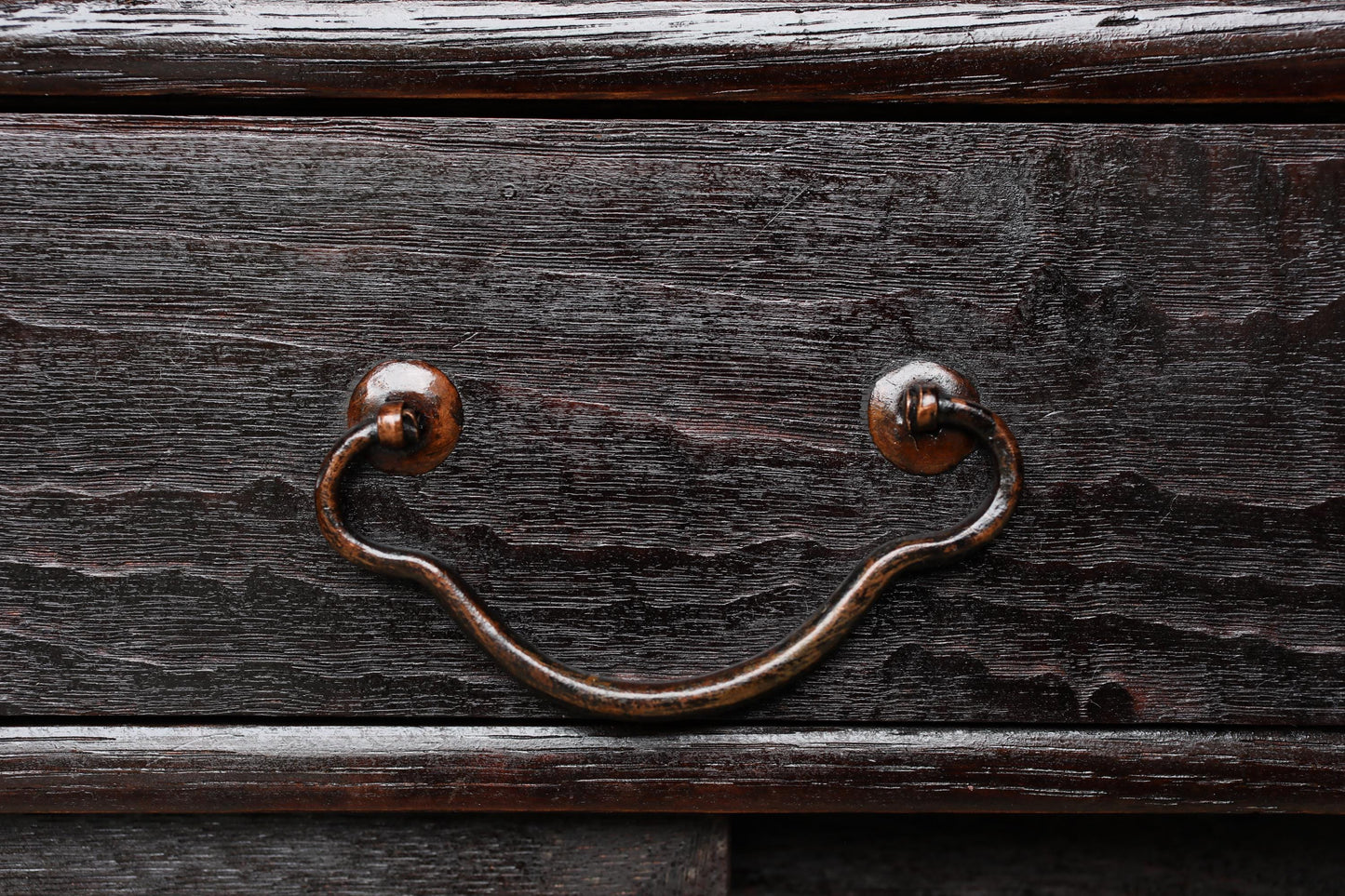 a close-up view of a dark wooden drawer with a curved metal handle.