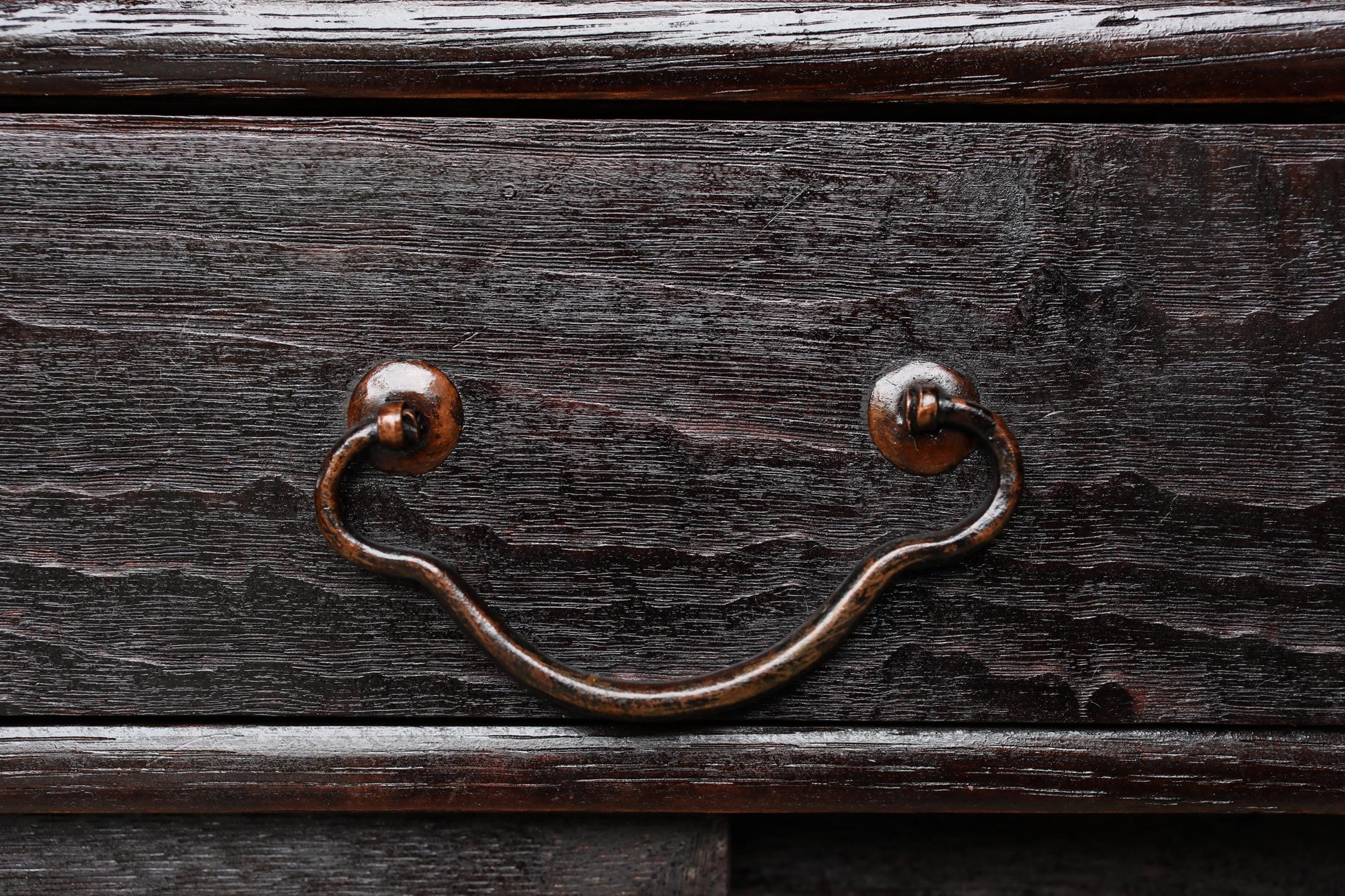 a close-up view of a dark wooden drawer with a curved metal handle.