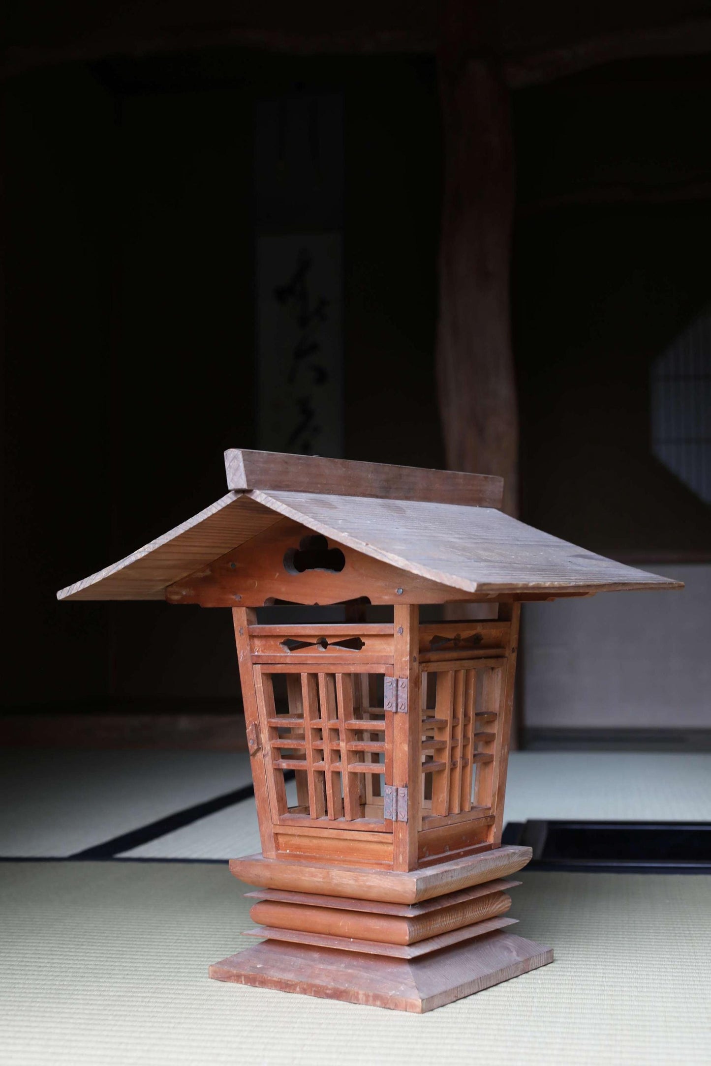 A wooden lantern with a sloping roof sits on a tatami mat in a dimly lit room.