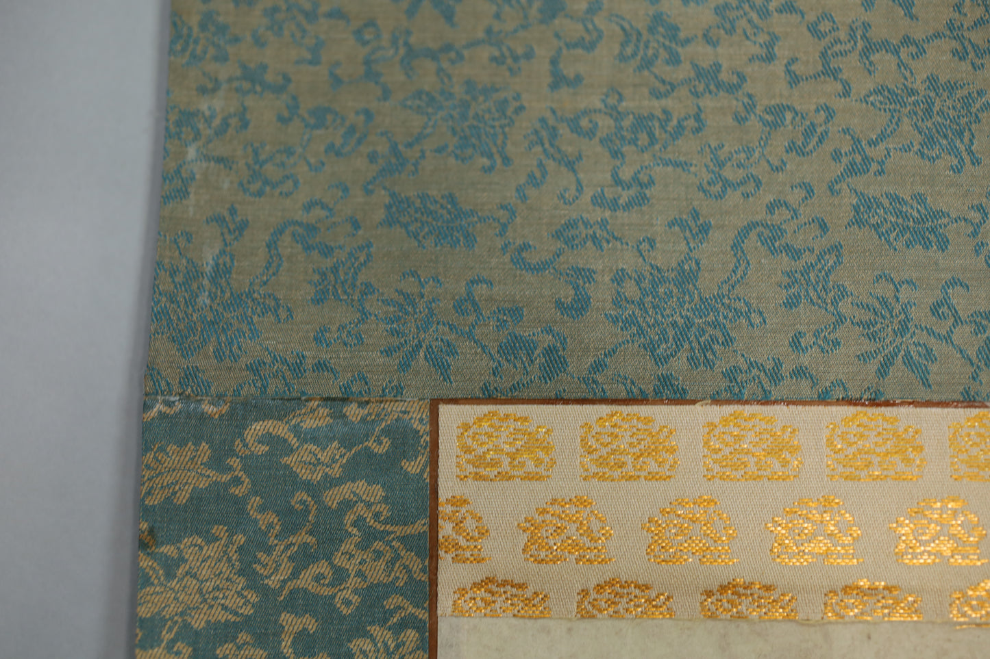 a close-up view of a fabric with a floral pattern in shades of blue and green, and a gold-colored fabric with a repeating pattern of small flowers or leaves.