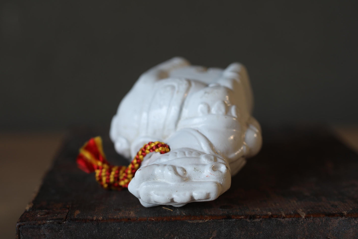 A white ceramic figurine with a red and yellow string tied around it, placed on a wooden surface.