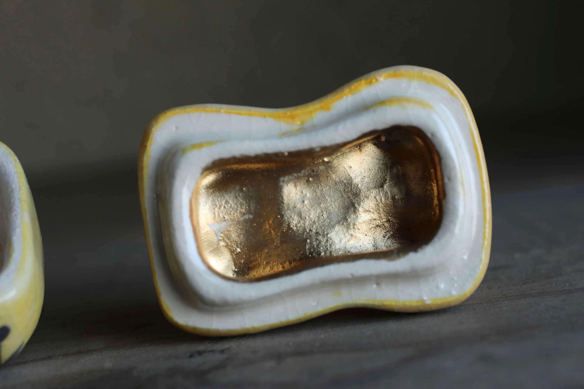 a close-up view of a ceramic object with a gold-colored interior, resting on a surface.