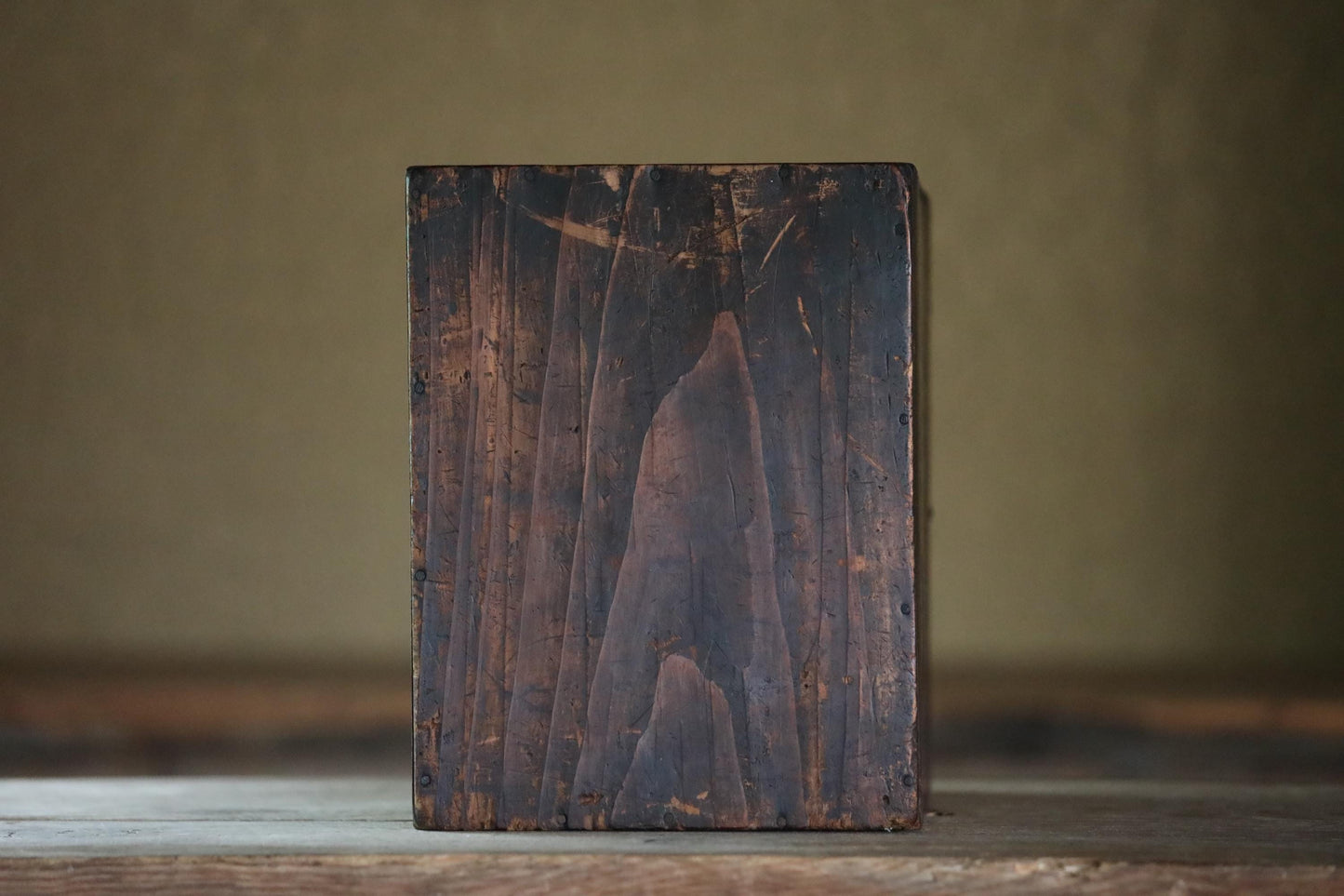 a wooden block or block of wood with a weathered, dark brown surface, sitting on a wooden surface.