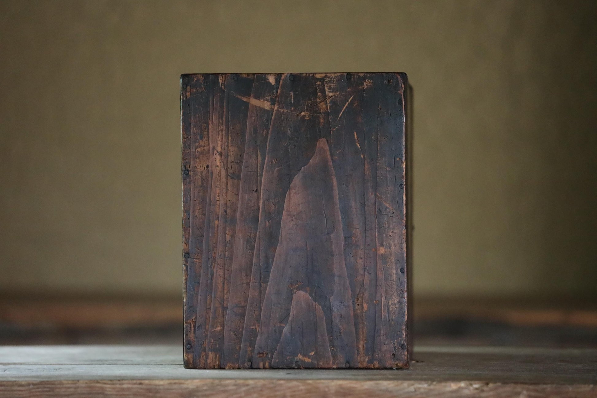 a wooden block or block of wood with a weathered, dark brown surface, sitting on a wooden surface.