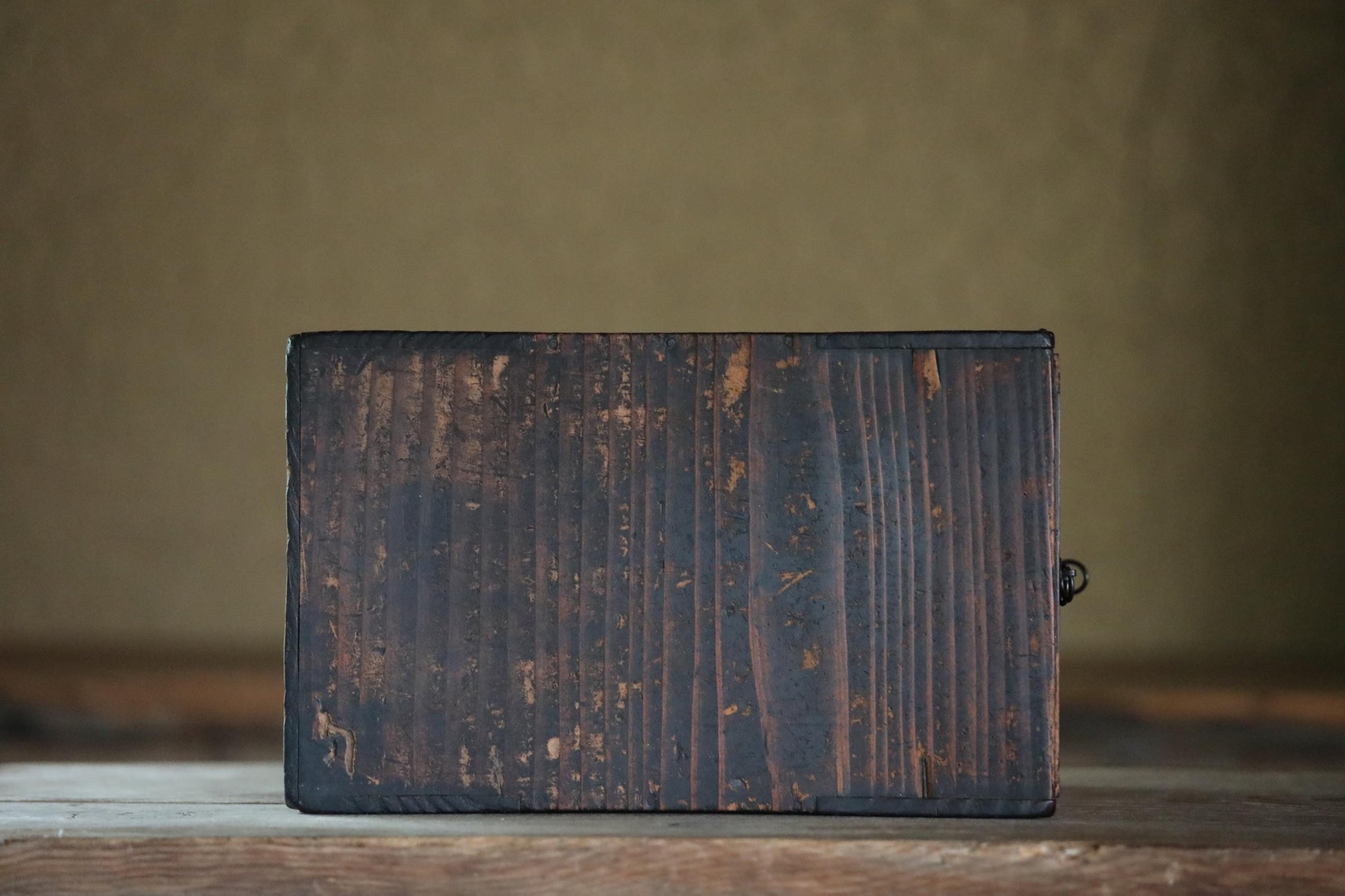 A weathered, dark wooden surface sits on a wooden surface, with a blurred background.