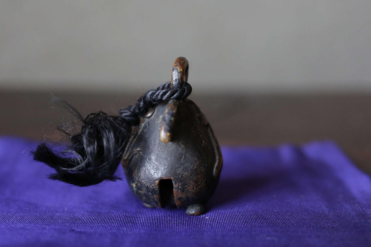 A small, black metal bell with a tassel hanging from it, resting on a purple surface.