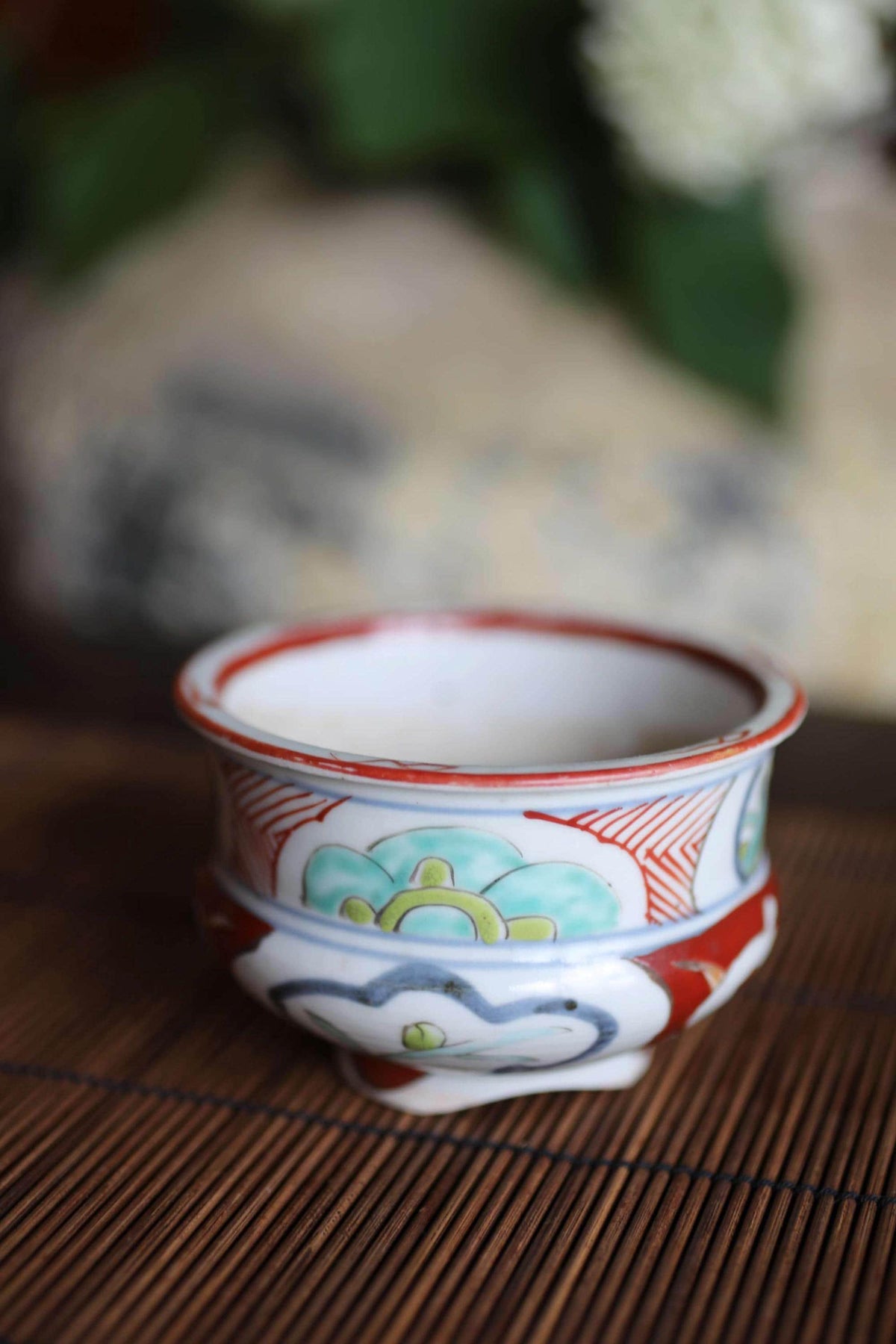 A ceramic bowl with a colorful floral design sits on a bamboo mat.