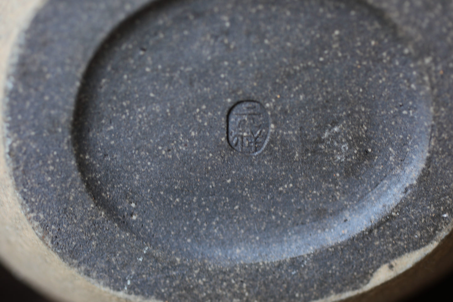 A close-up image of a dark, textured surface with a small, circular symbol or mark in the center.