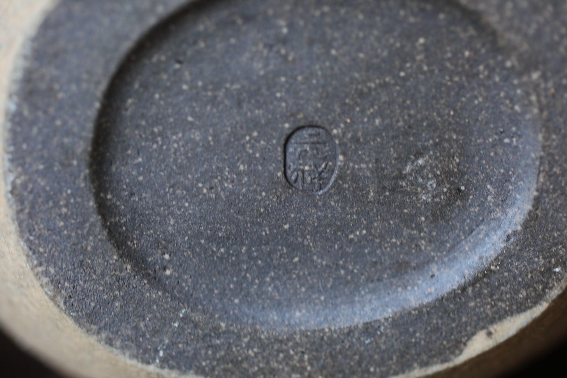 A close-up image of a dark, textured surface with a small, circular symbol or mark in the center.