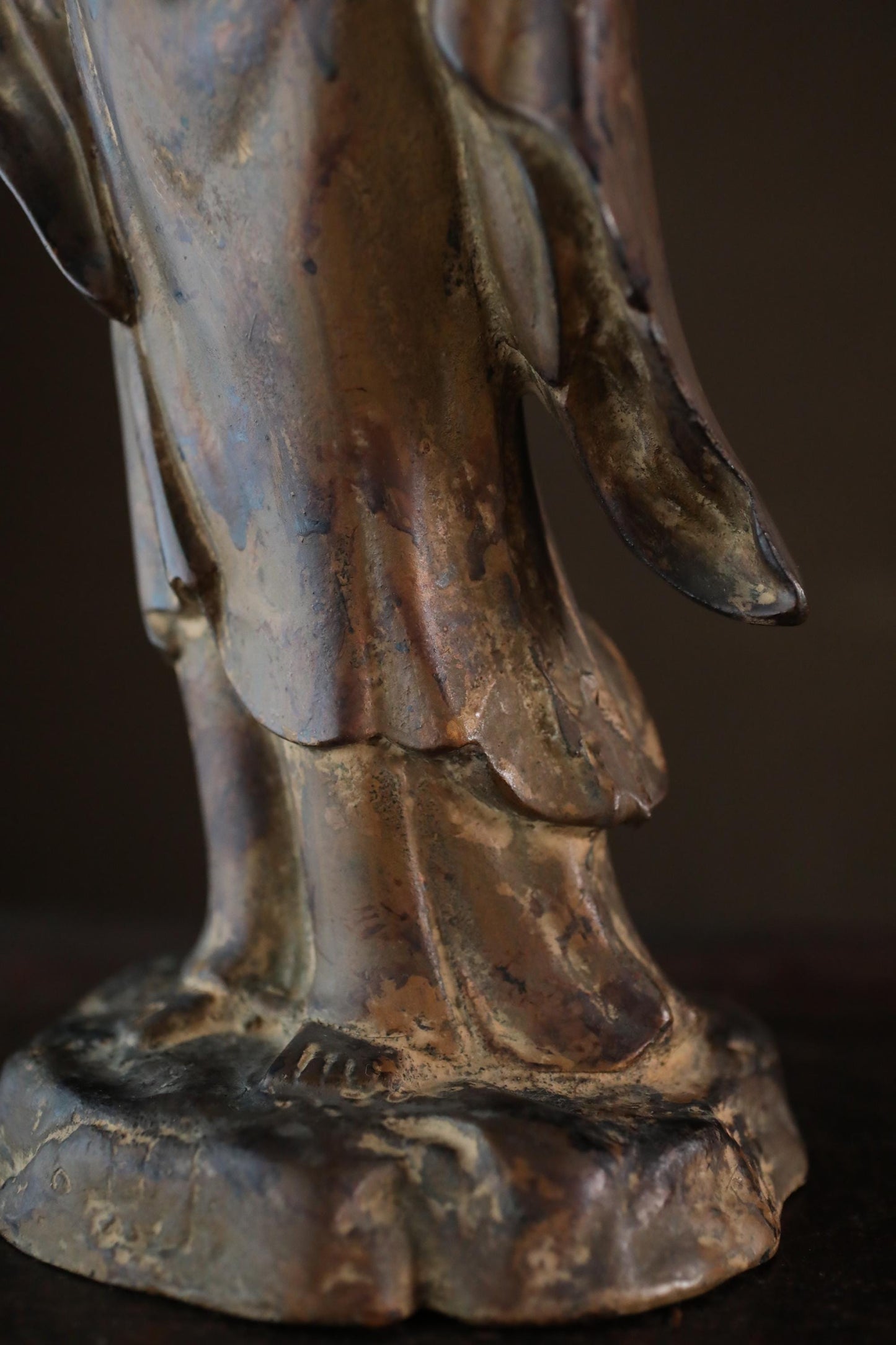 A close-up view of a bronze statue depicting a figure with a flowing robe and a pointed hat, set against a dark background.