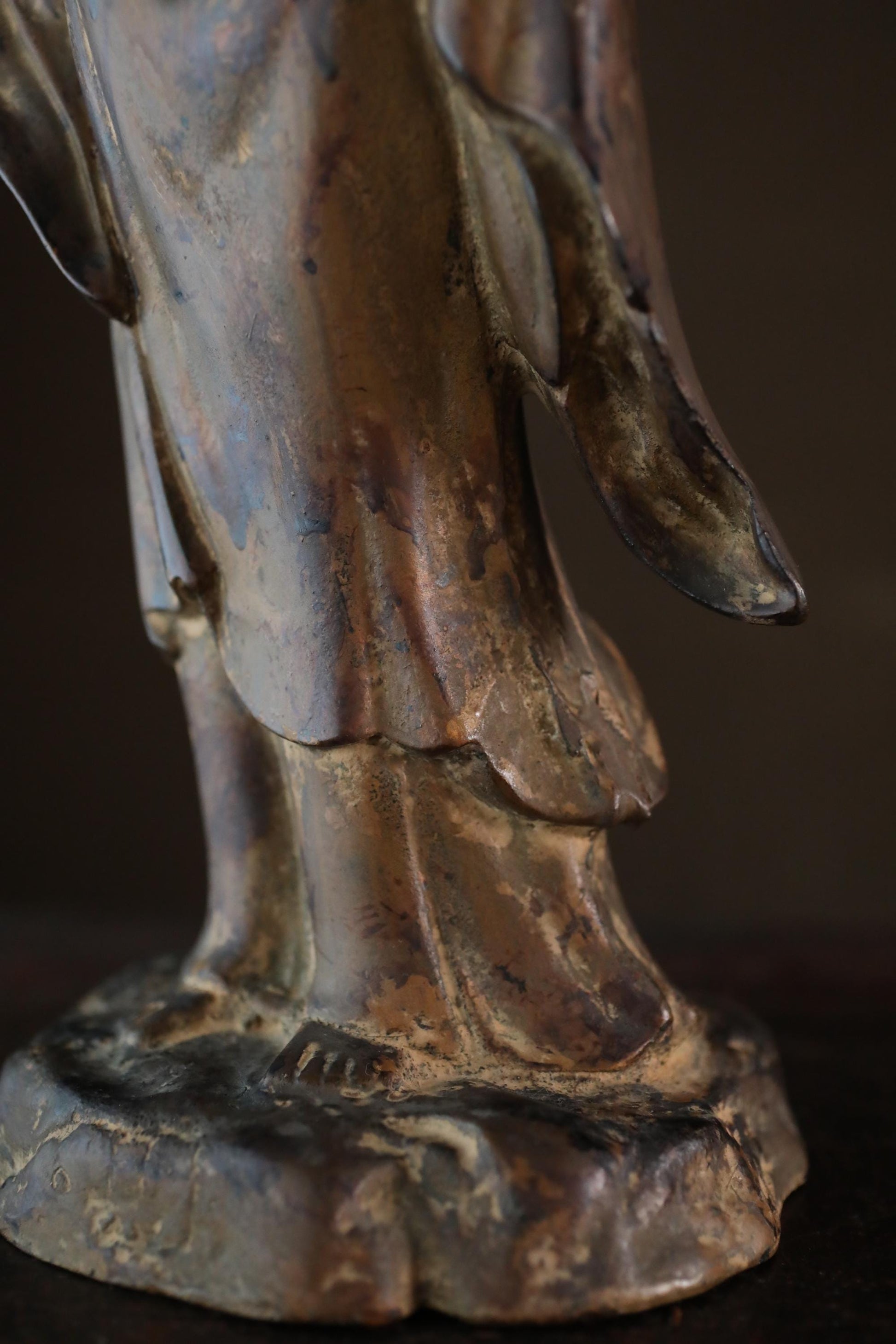 A close-up view of a bronze statue depicting a figure with a flowing robe and a pointed hat, set against a dark background.