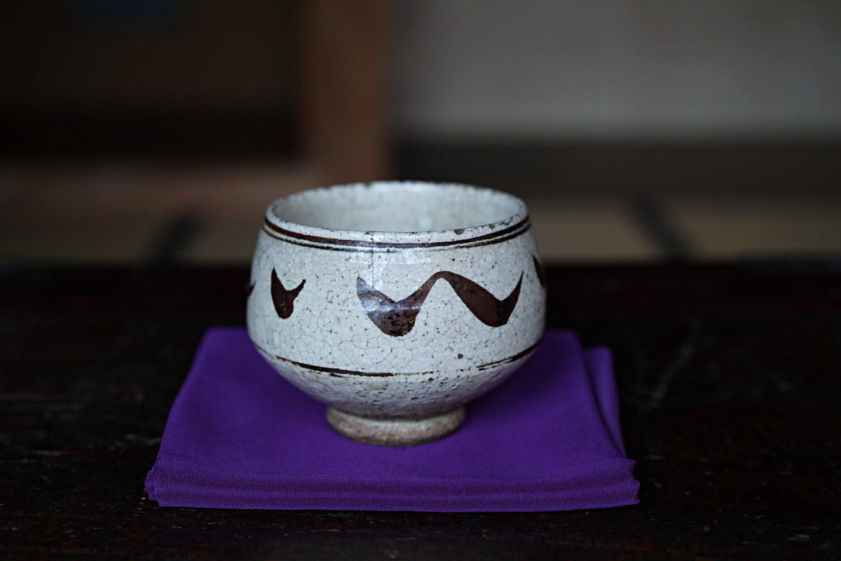 A white ceramic bowl with a decorative design sits on a purple cloth on a dark wooden surface.
