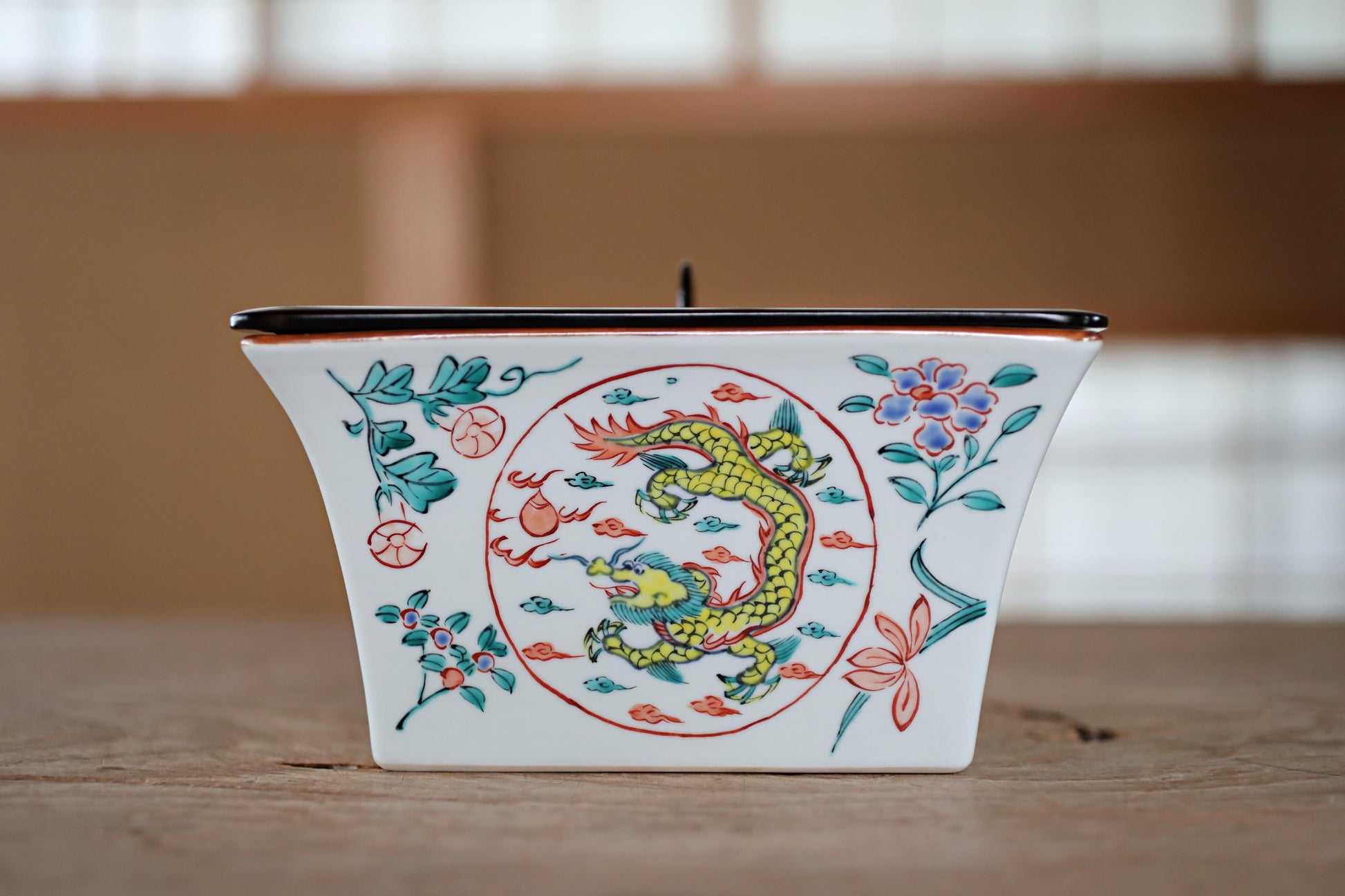 A ceramic container with a dragon design on it, placed on a wooden surface.
