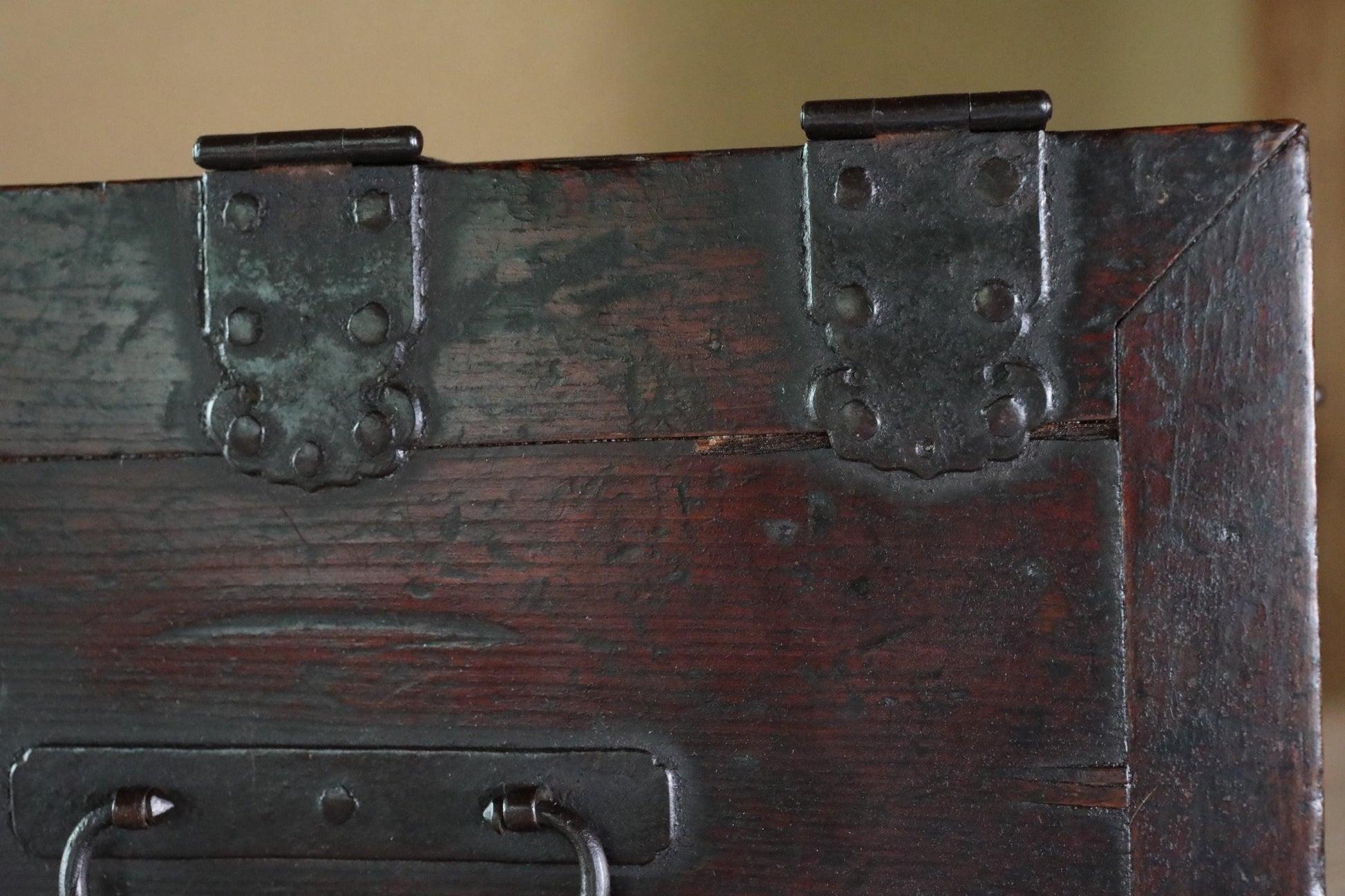 a close-up view of a dark wooden surface with metal hinges and handles, giving it a vintage or antique appearance.