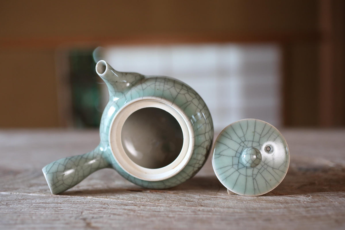 A ceramic teapot with a white interior and a green exterior sits on a wooden surface, with the lid and spout visible.