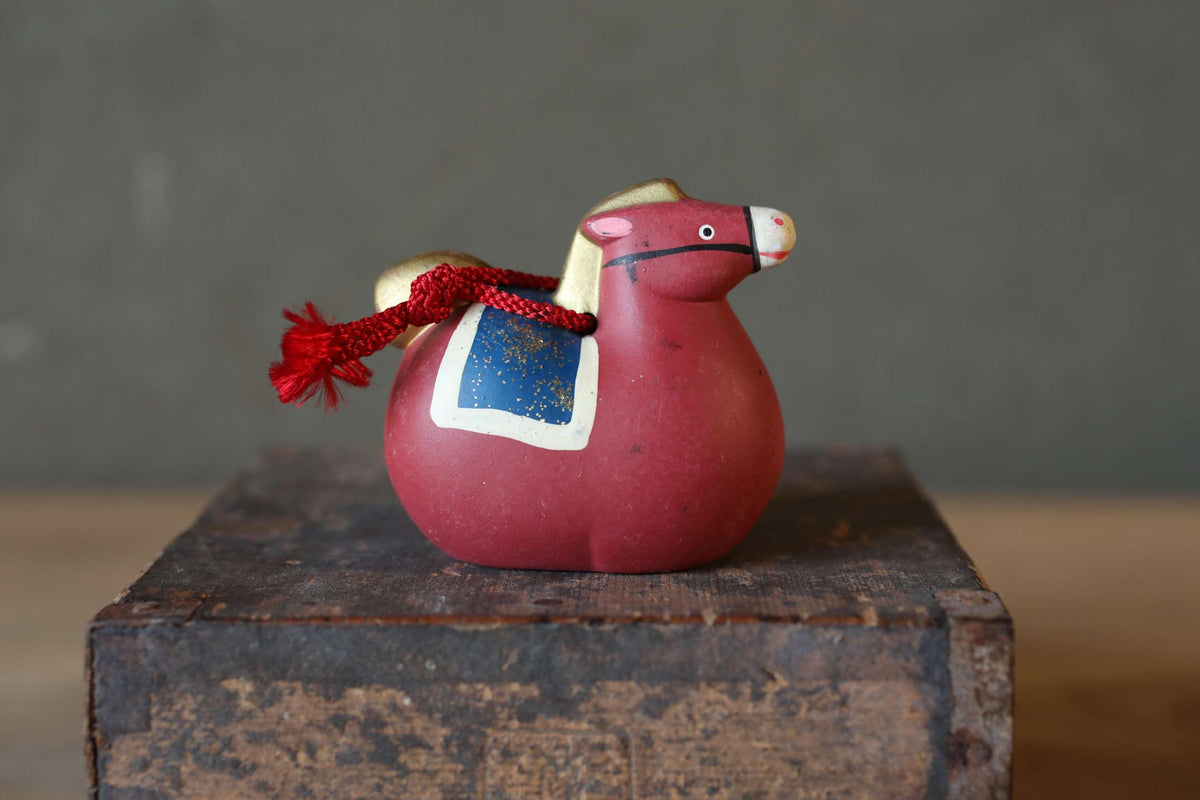 A small red ceramic horse figurine with a blue and white design on its side, sitting on a wooden surface.