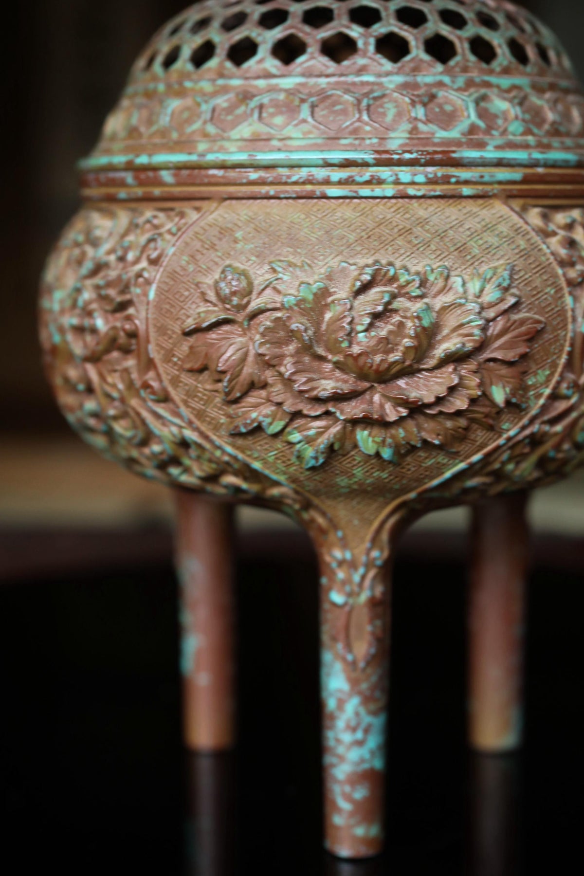 A close-up image of a decorative metal object, possibly a vase or urn, with intricate floral designs and a textured surface.