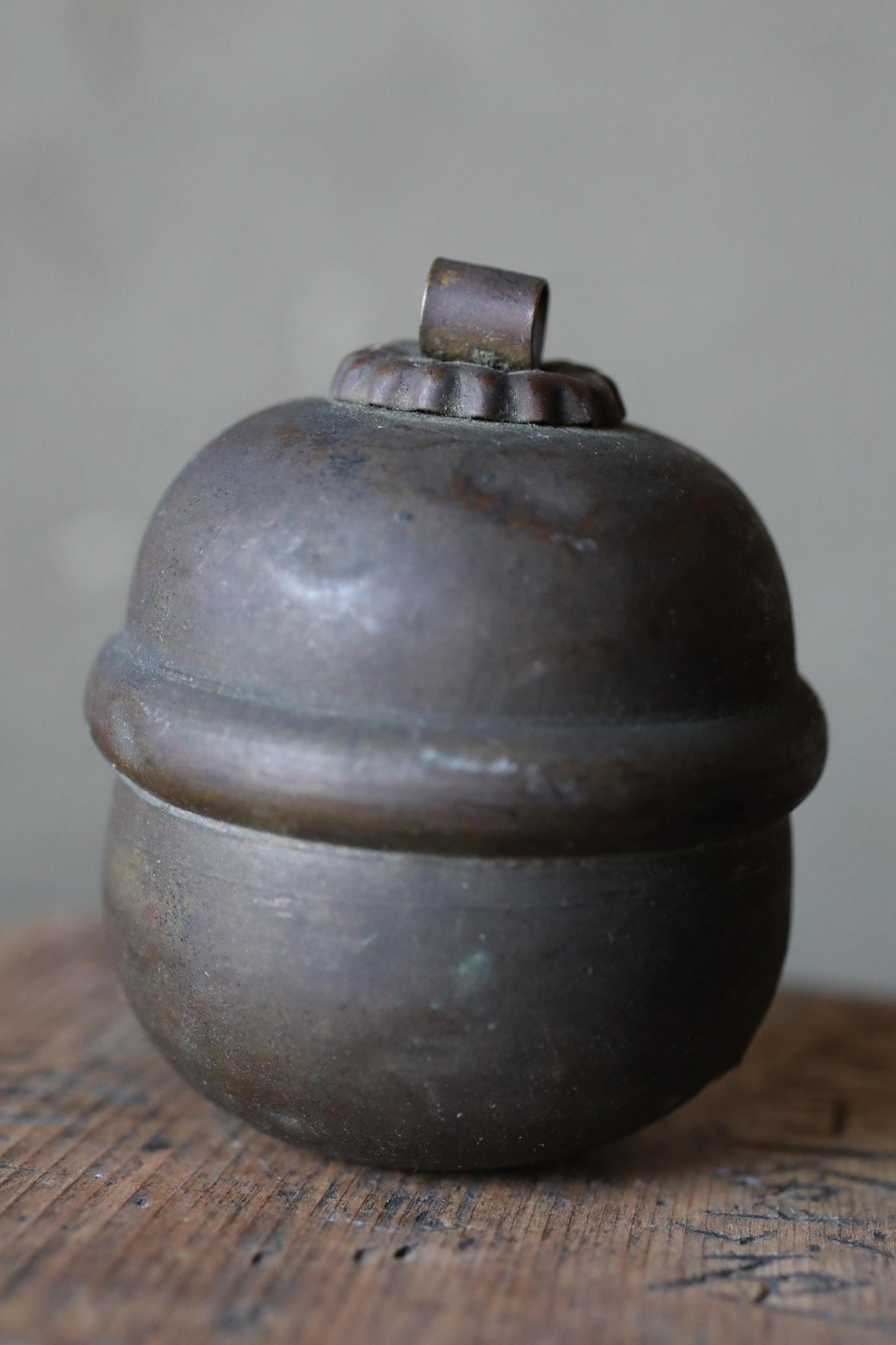 A round, dark-colored metal container with a small, rusted-looking top piece on top.