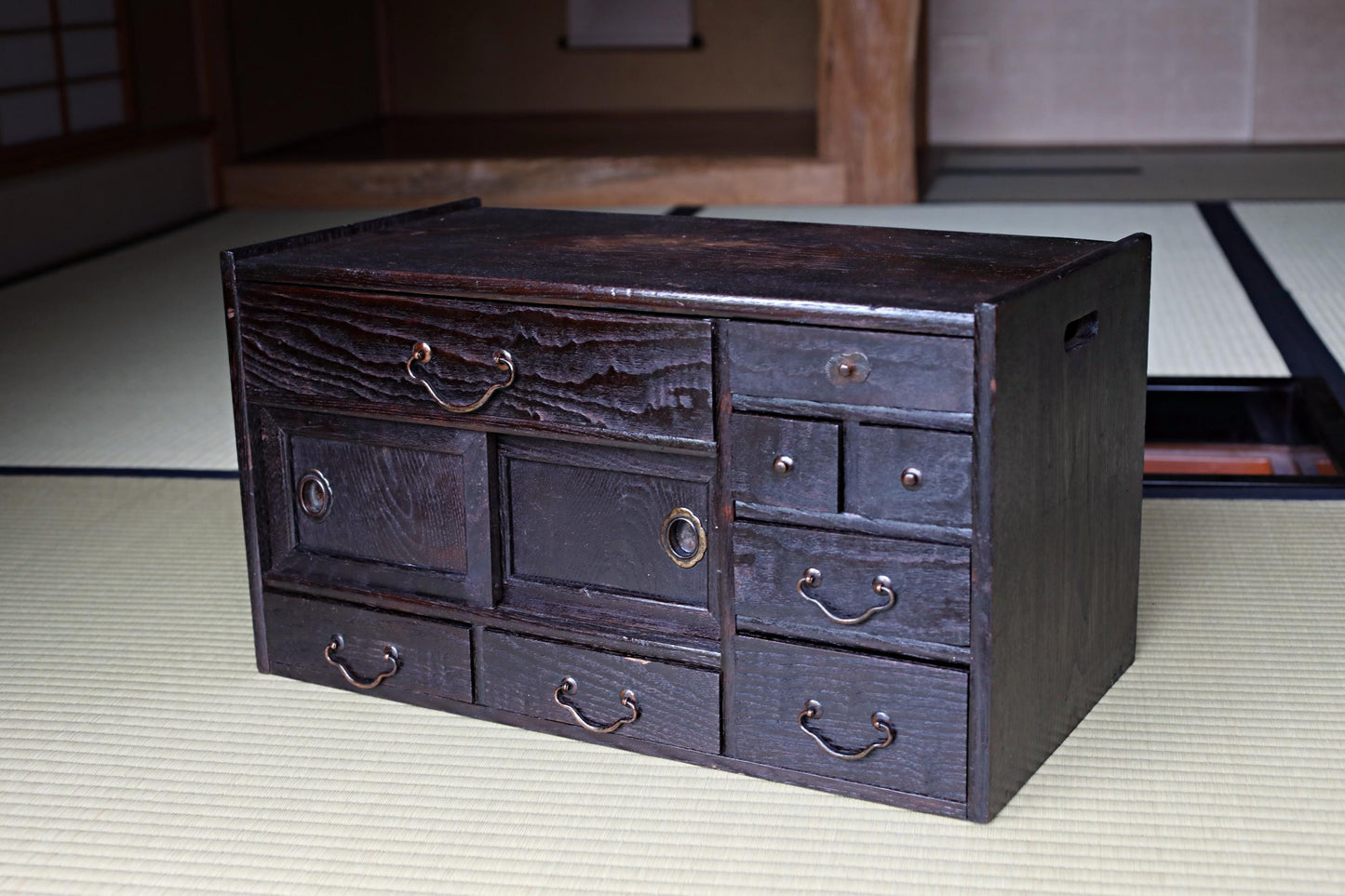 A dark wooden cabinet with multiple drawers and doors, sitting on a beige mat.