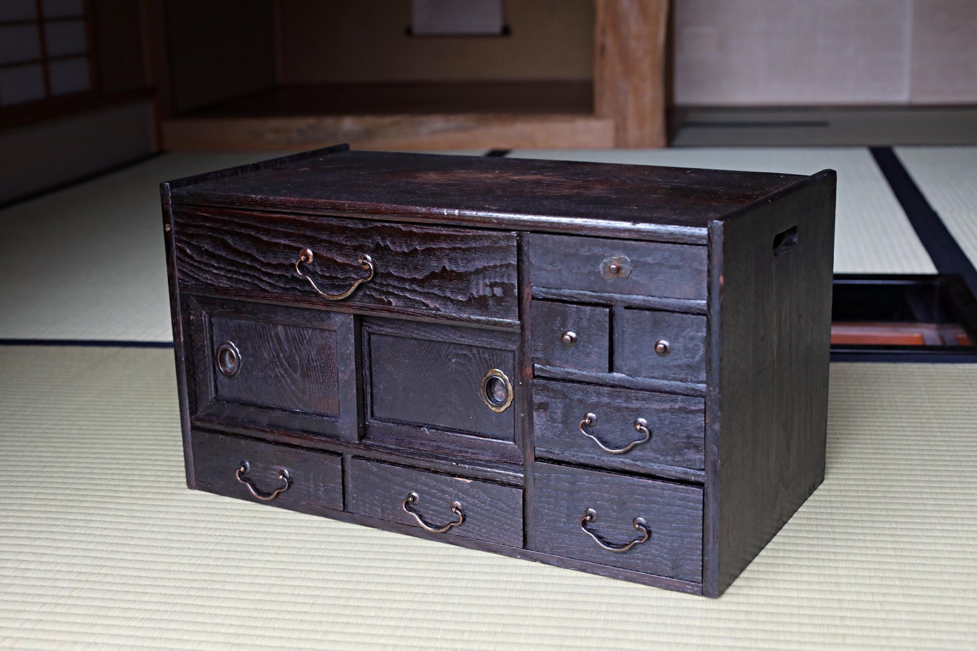 A dark wooden cabinet with multiple drawers and doors, sitting on a beige mat.