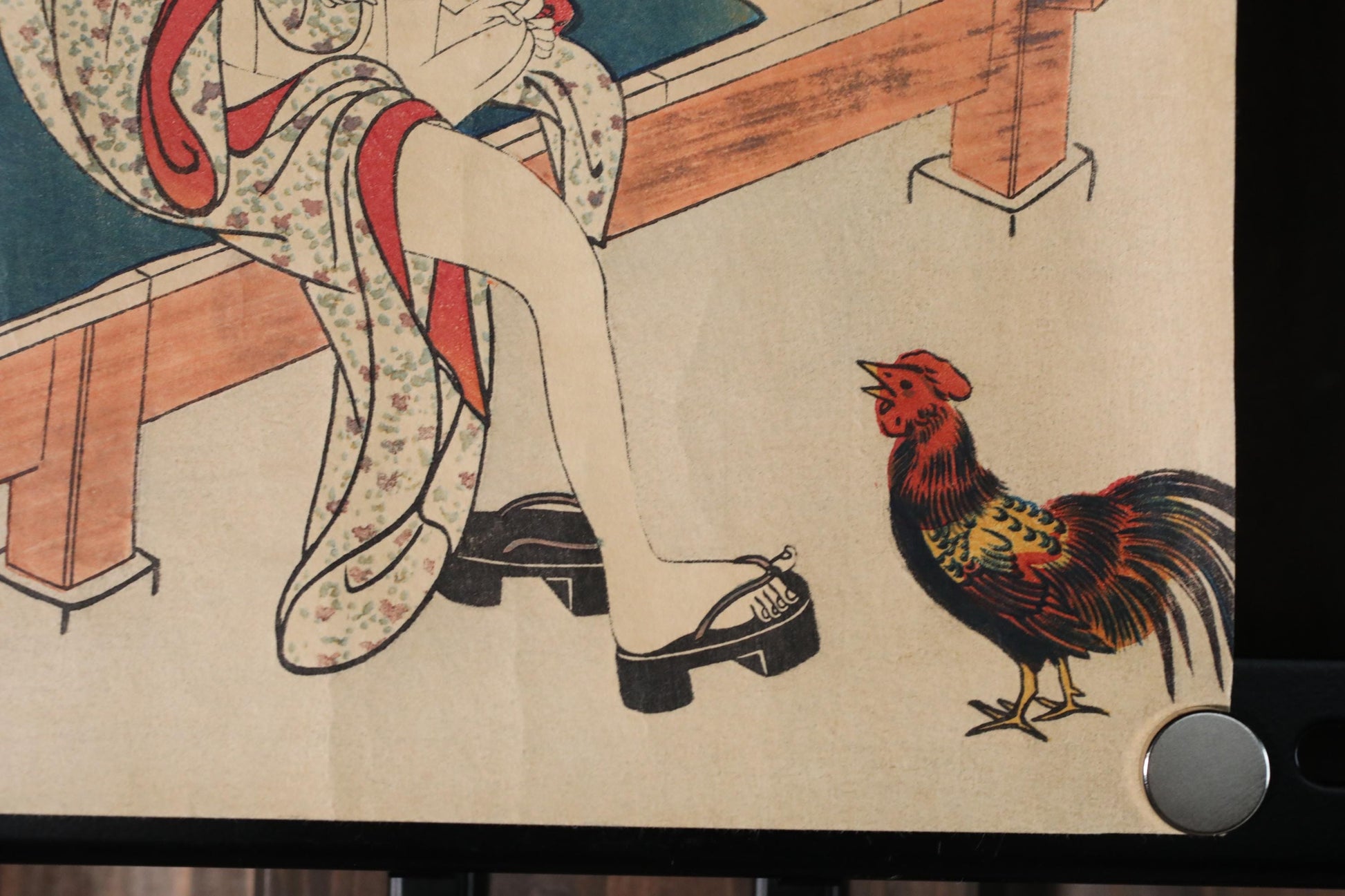 A close-up of a traditional Japanese woodblock print depicting a woman in a kimono sitting on a bench, with a rooster standing next to her feet.