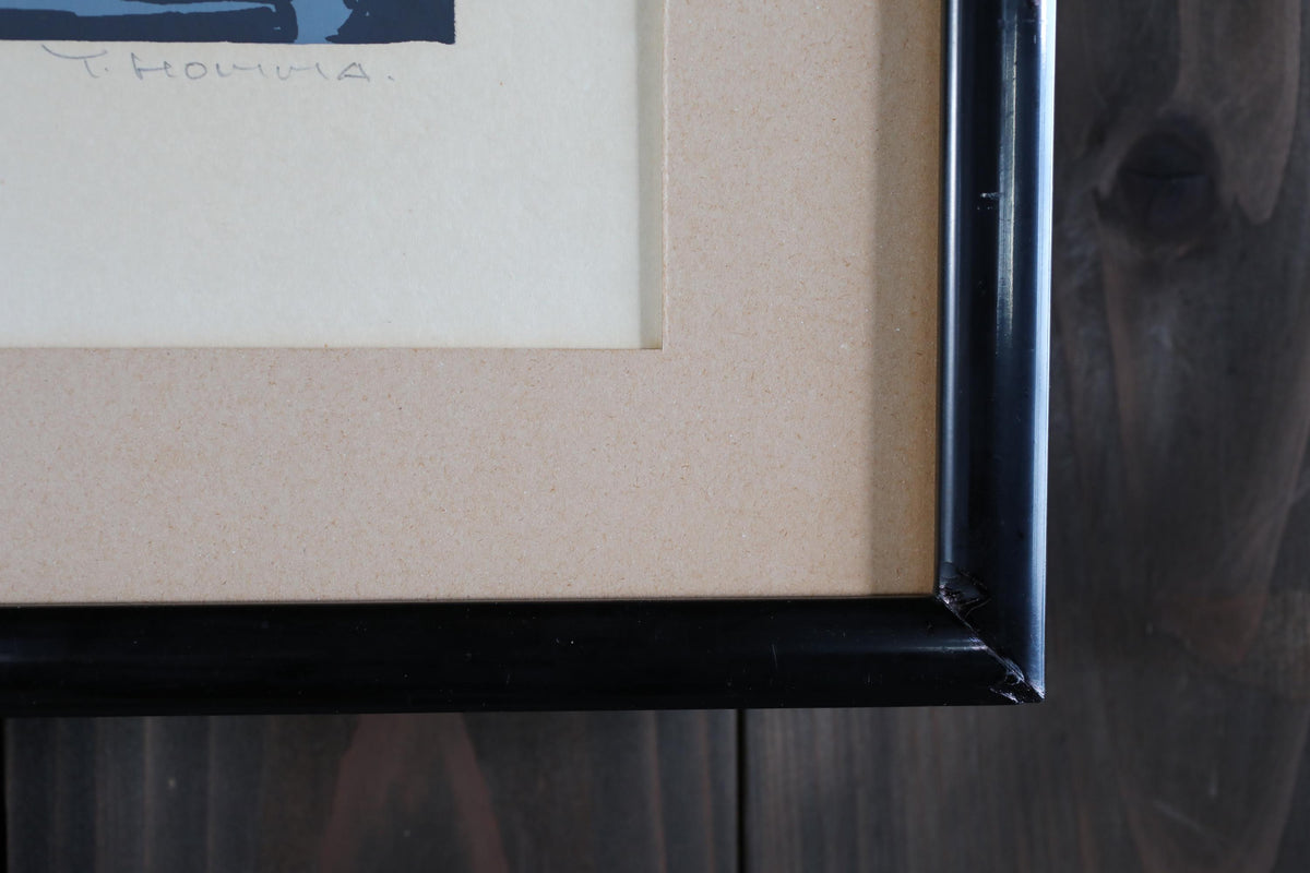 a close-up view of a framed artwork with a black border, placed on a wooden surface.