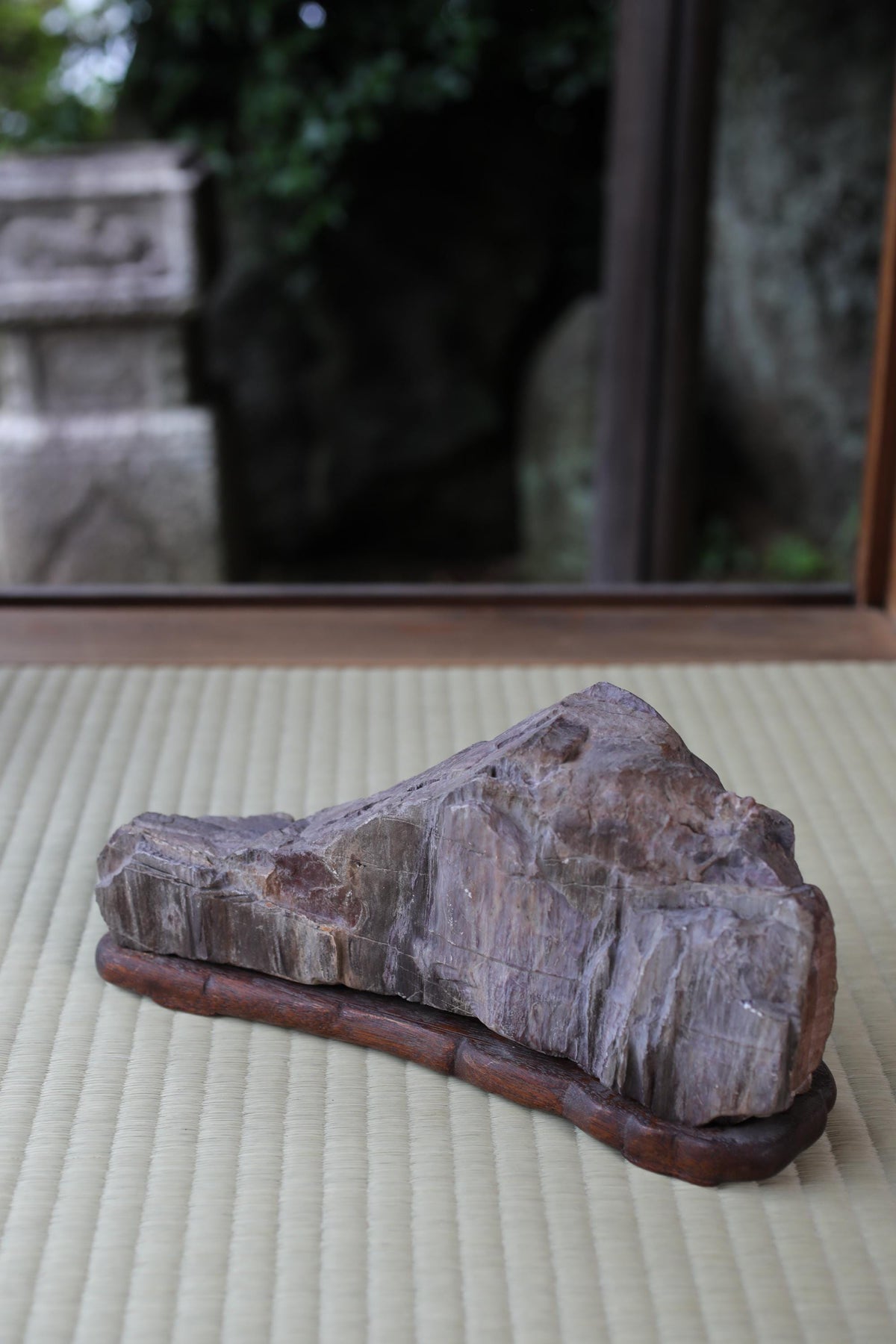 a large, irregularly shaped rock sitting on a wooden base, placed on a woven mat.