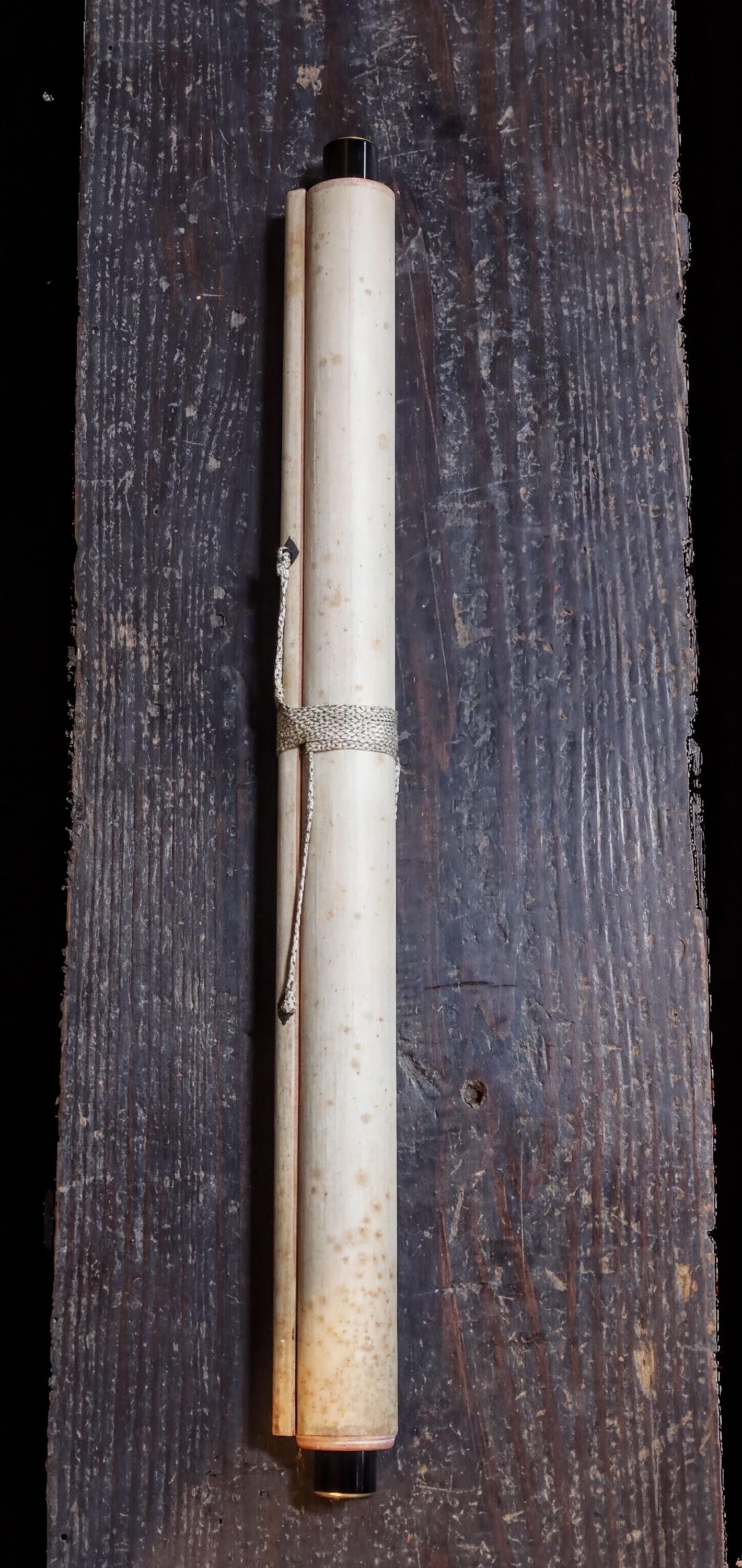 A white scroll with a black tip is tied with a string and placed on a wooden surface.