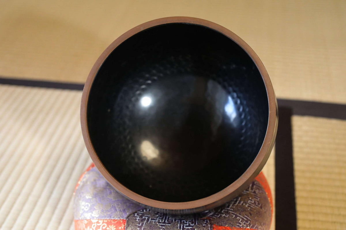 a black bowl with a brown rim, placed on a colorful, patterned surface.