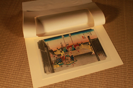 The image is an open book with a printed page featuring an illustration of a city scene with people and buildings.