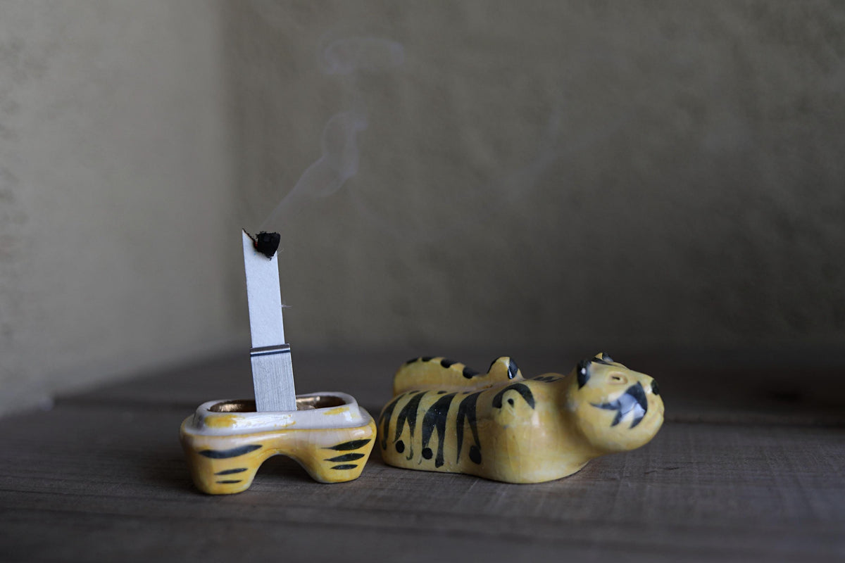 A ceramic tiger figurine is shown with a lit cigarette inserted into its mouth, emitting smoke.