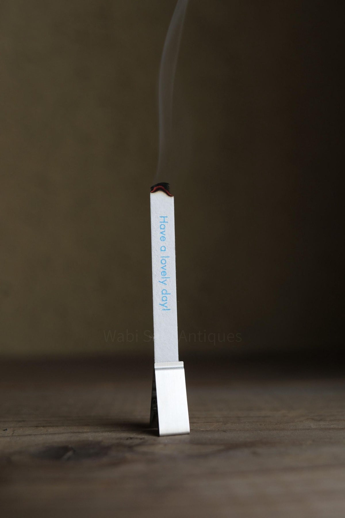 A single matchstick is standing upright on a wooden surface, with smoke rising from it.
