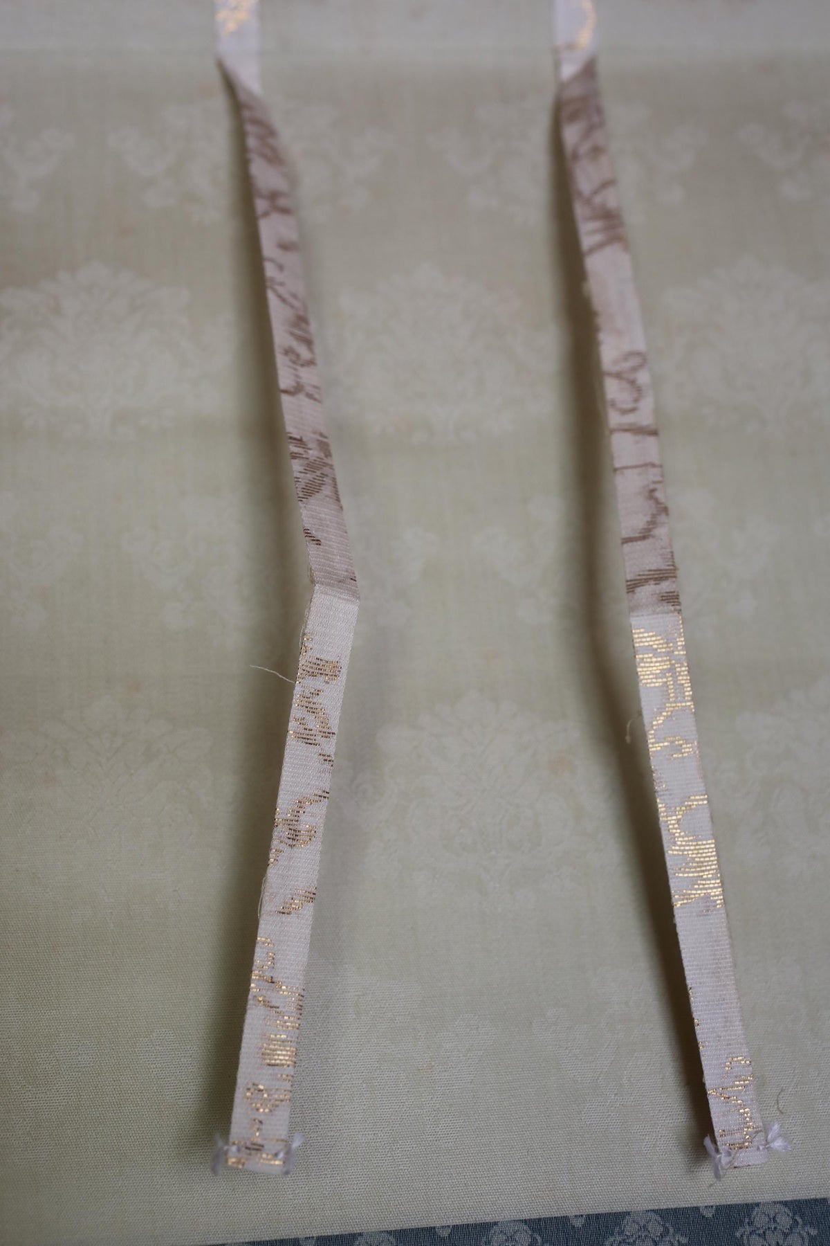 two white ribbons with gold floral patterns, placed side by side on a beige background.