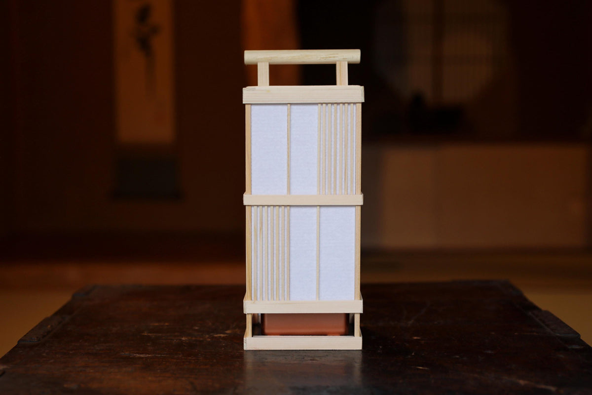 A wooden lantern with a white paper shade is placed on a dark wooden surface.