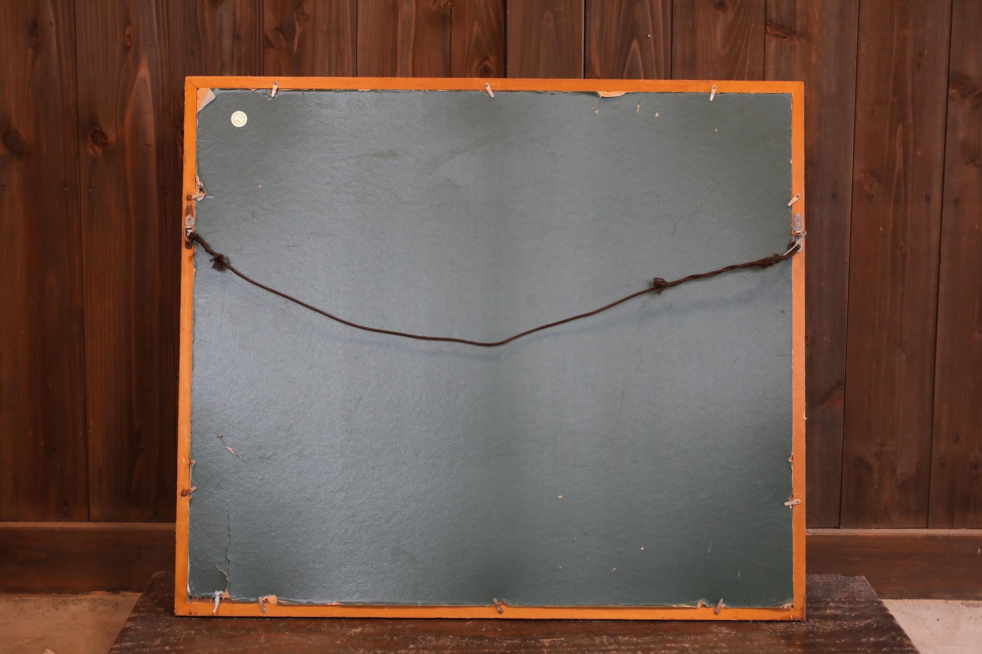 a wooden frame with a black background, and a string or wire attached to the back of the frame.