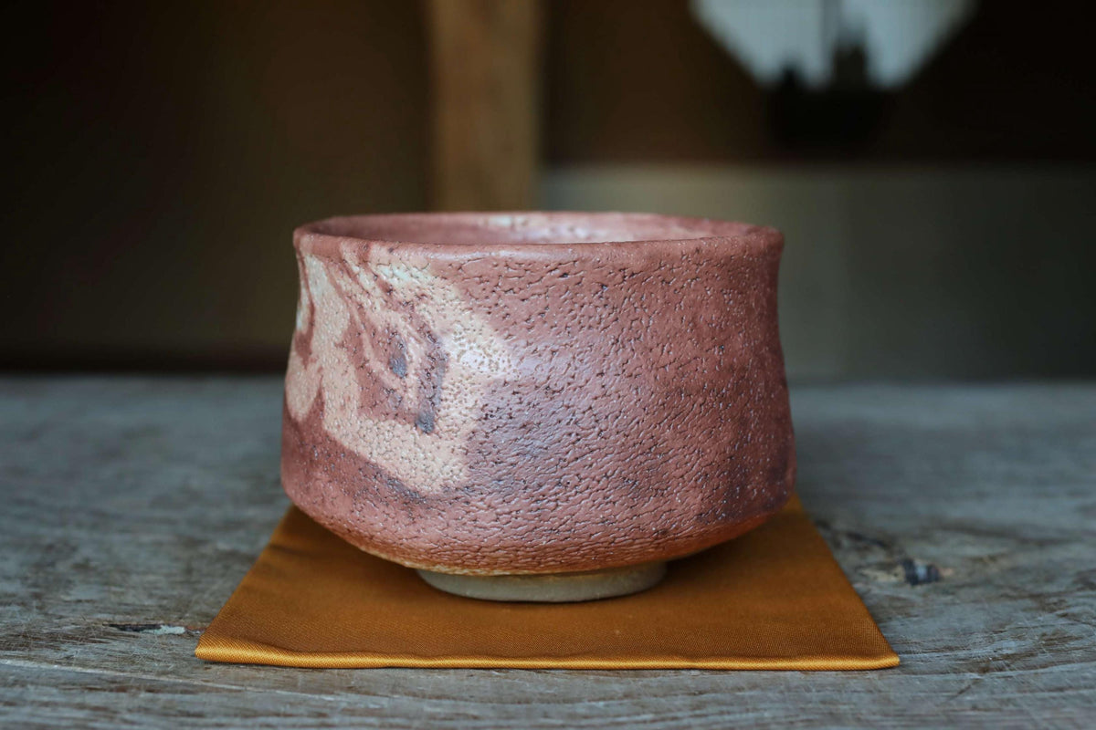 A ceramic bowl with a reddish-brown hue sits on a wooden surface, with a blurred background.