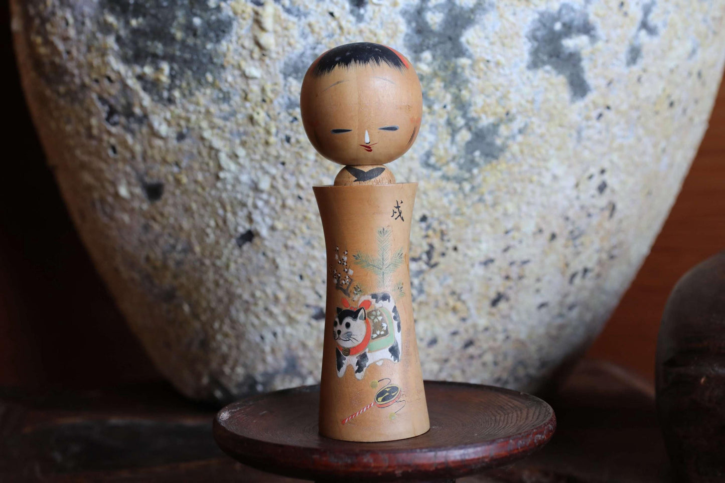 A wooden figurine of a person with a cat on their lap, sitting on a wooden stand.