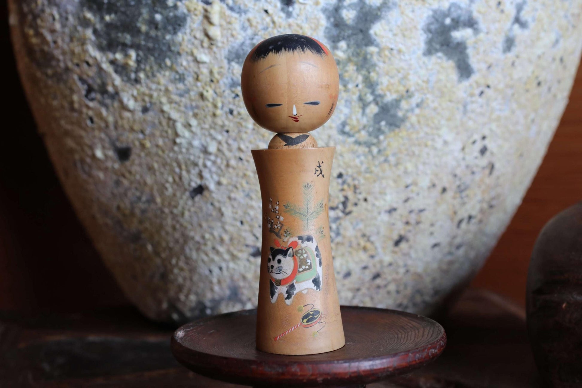 A wooden figurine of a person with a cat on their lap, sitting on a wooden stand.